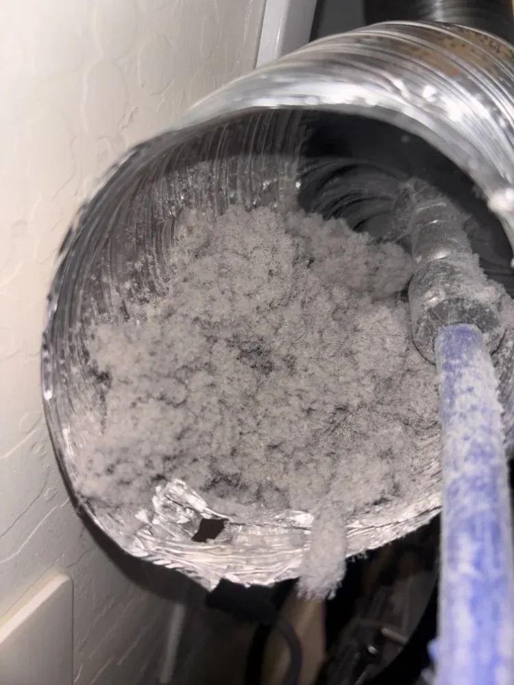 Inside a dryer duct showing packed lint with a cleaning brush inserted